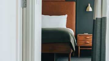 Et hotelværelse med en seng, et natbord, en lampe og udsigt gennem en åben dør.