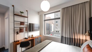 Una habitación de hotel moderna con cama, escritorio y un amplio ventanal con cortinas.