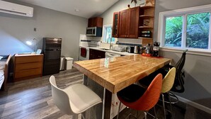 A modern kitchen with wooden cabinetry, a central island, and a view of greenery outside. - A private newly renovated cabin surrounded by trees (Lake Forest Park)