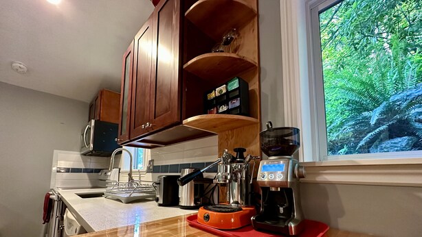 A kitchen with wooden cabinets, a coffee machine, a toaster, and a window with a view of greenery. - A private newly renovated cabin surrounded by trees (Lake Forest Park)