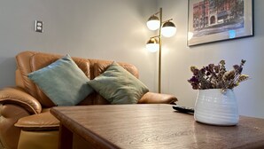 A living room with a leather sofa, a wooden coffee table, a vase with dried flowers, a floor lamp, and a framed picture on the wall. - A private newly renovated cabin surrounded by trees (Lake Forest Park)