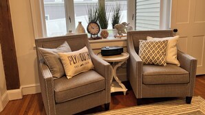 Two armchairs with decorative pillows, a small round table, and a window with blinds.