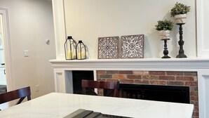 A modern kitchen with a black induction cooktop, white marble countertop, and a white mantel above the fireplace.