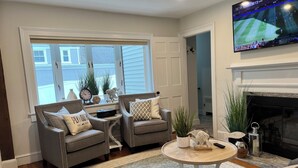 A living room with two armchairs, a coffee table, a fireplace, and a TV mounted on the wall.