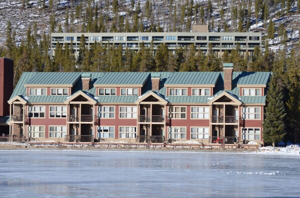 A multi-story hotel with a green roof, located near a frozen lake with a backdrop of trees and a mountain. - Ski mountain & Lake Views -Resort Shuttle, Keystone Convention Center - 2 BR (Keystone)