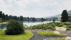 Vista sul lago con un sentiero lastricato, aree verdi e una fila di edifici sullo sfondo.