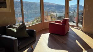 Una habitación de esquina con un ventanal grande, una silla roja, un sofá oscuro y piso de madera.