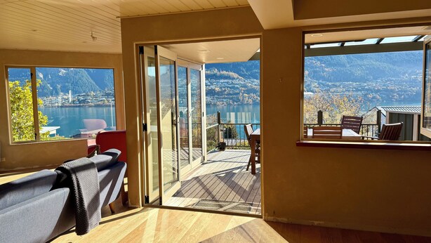 Una habitación con un amplio ventanal corredero que da a una terraza exterior con vistas a un lago y montañas.