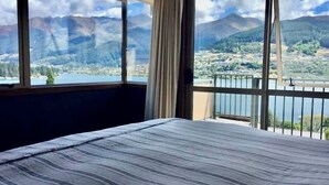 Una habitación con cama, ventanas amplias y vistas a montañas y un lago.