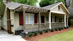 A two-story house with a covered porch, a brick chimney, and a small front yard with mulch and shrubs.