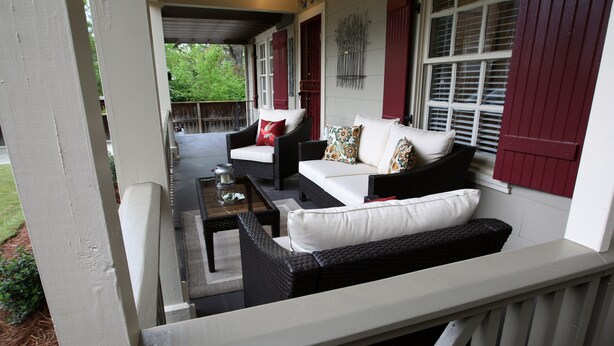A covered porch with wicker furniture, a coffee table, and a view of the garden.