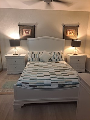Een slaapkamer met een bed, twee nachtkastjes, twee wandlampen en twee prenten in lijst.