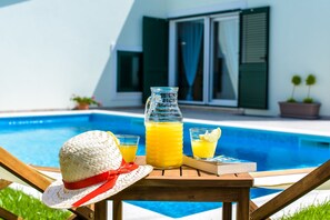 A poolside setting with a wooden table, a straw hat, a book, and a glass bottle of orange juice. - Gracefully villa Lucia **** (Mravince)