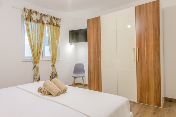 A bedroom with a bed, a chair, a TV mounted on the wall, and wooden wardrobes. - Gracefully villa Lucia **** (Mravince)