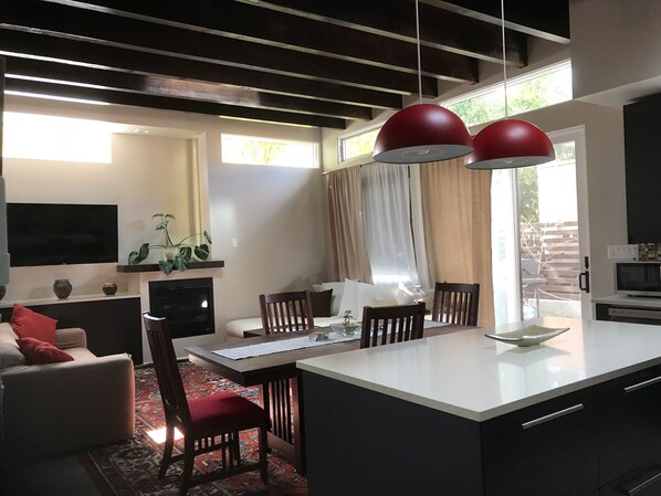 A modern kitchen with a dining area, featuring a large island, red pendant lights, and a flat-screen TV mounted on the wall. - Truly unique art-filled home w/ garden close to the Plaza. (SANTA FE)
