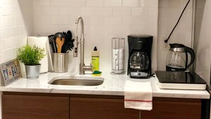 Ett kök med en diskho i rostfritt stål, träskåp, en kaffebryggare och en växt.