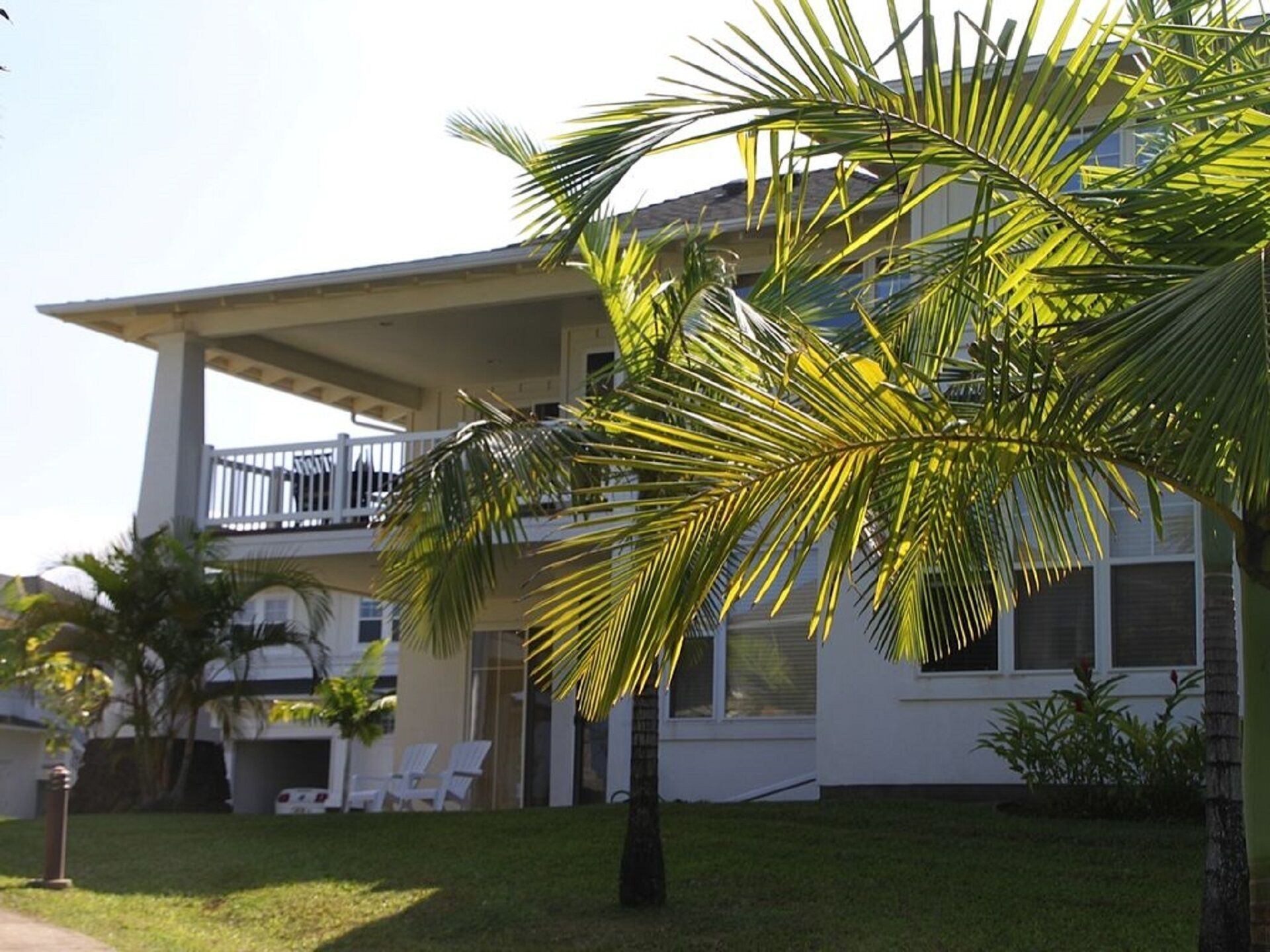 A two-story house with a balcony, a lawn, and a palm tree.