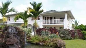 A two-story house with a waterfall feature in the front yard. - Gorgeous, 3 private suites. Balcony View, Pool, Fitness Center! (Princeville)