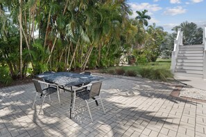 An outdoor patio with a metal table and chairs, surrounded by lush greenery and palm trees.