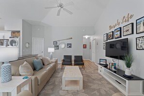 A modern living room with a beige sofa, a coffee table, a TV, and a wall with framed pictures.