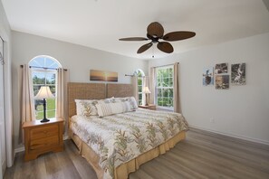 A bedroom with a large bed, two bedside tables, a ceiling fan, and a window with curtains.