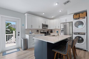 A modern kitchen with white cabinets, stainless steel appliances, a central island with bar stools, and a view of the outdoors. - Hidden Treasure is ready for your stay (Fort Myers Beach)