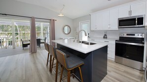 A modern kitchen with white cabinets, stainless steel appliances, and a large island with bar stools. - Hidden Treasure is ready for your stay (Fort Myers Beach)