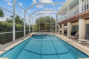 A swimming pool with a sun deck area, surrounded by palm trees and a clear sky.