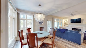 A dining area with a round table and chairs, a chandelier, and a living room with a sofa and fireplace.