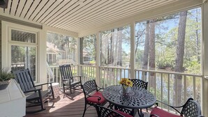 A covered outdoor deck with a table and chairs, overlooking a wooded area.