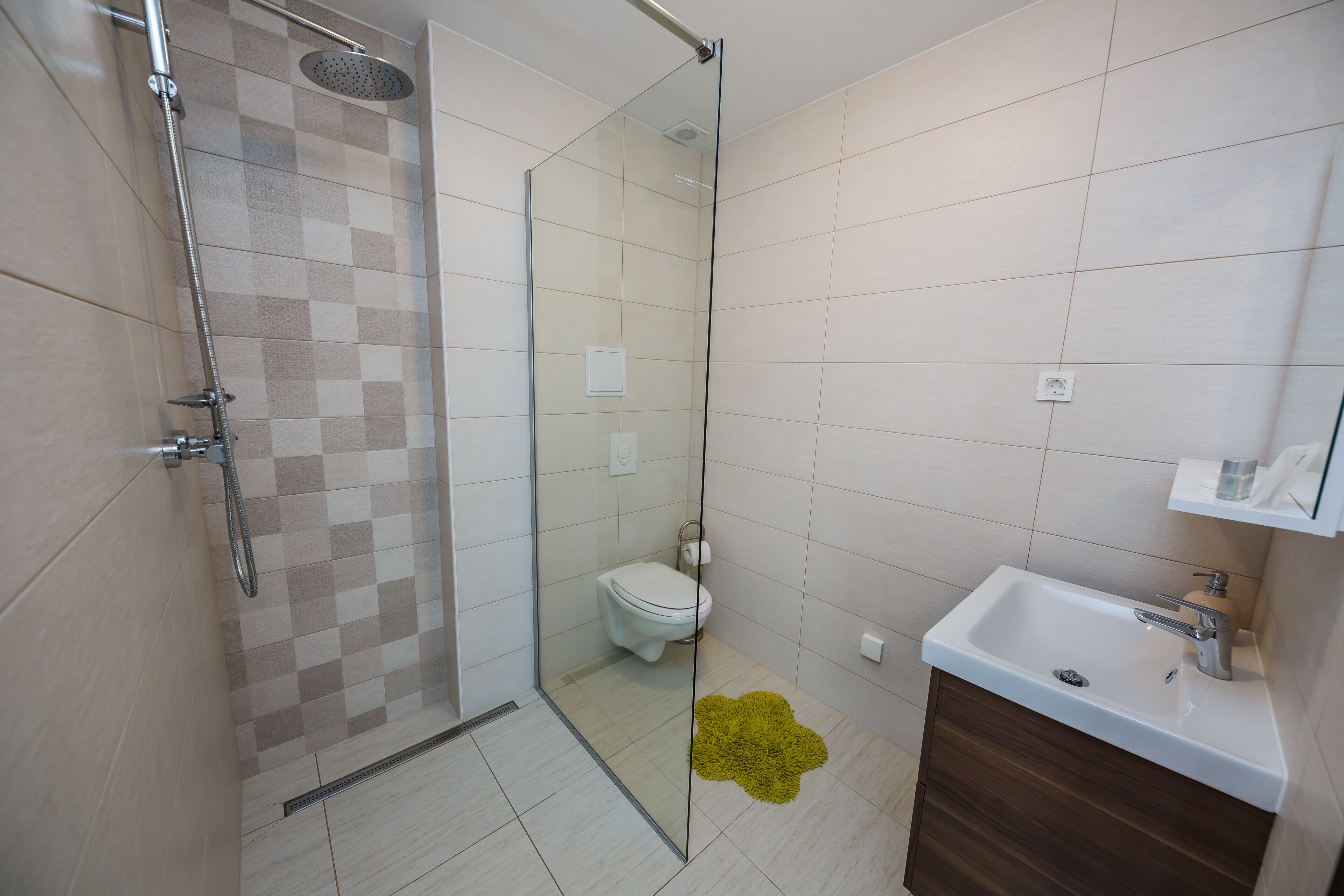 Un baño moderno con cabina de ducha de vidrio, inodoro blanco y lavabo con mueble de madera.