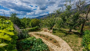 A garden with a stone pathway, a wooden bench, and a table. - Cherry Tree With Pool Near Split (Donje Sitno)