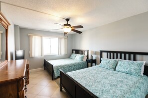 Une chambre avec deux lits, un ventilateur de plafond, une commode et une fenêtre avec des stores.