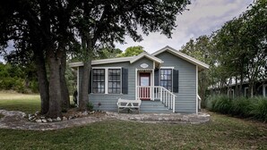 A small, single-story house with a front porch, a red door, and a white bench. - Broadway Cottage | Convenient Country Location (Fredericksburg)