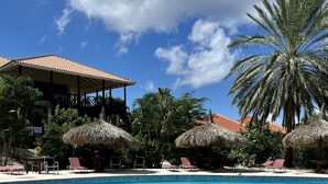 A swimming pool with lounge chairs and palm trees, surrounded by a building with a red roof. - ⭐ Blue Bay BEACH villa, minutes walk to beach/pool/golf⭐ 🧡 3BR/2BA (Blue bay golfresort)