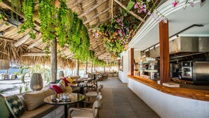 A restaurant with outdoor seating, a thatched roof, and hanging plants. - ⭐ Blue Bay BEACH villa, minutes walk to beach/pool/golf⭐ 🧡 3BR/2BA (Blue bay golfresort)
