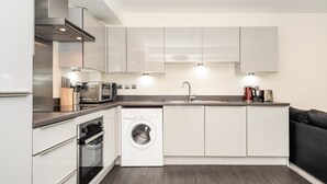 A compact kitchen with white cabinets, a built-in oven, a washing machine, and a coffee maker.