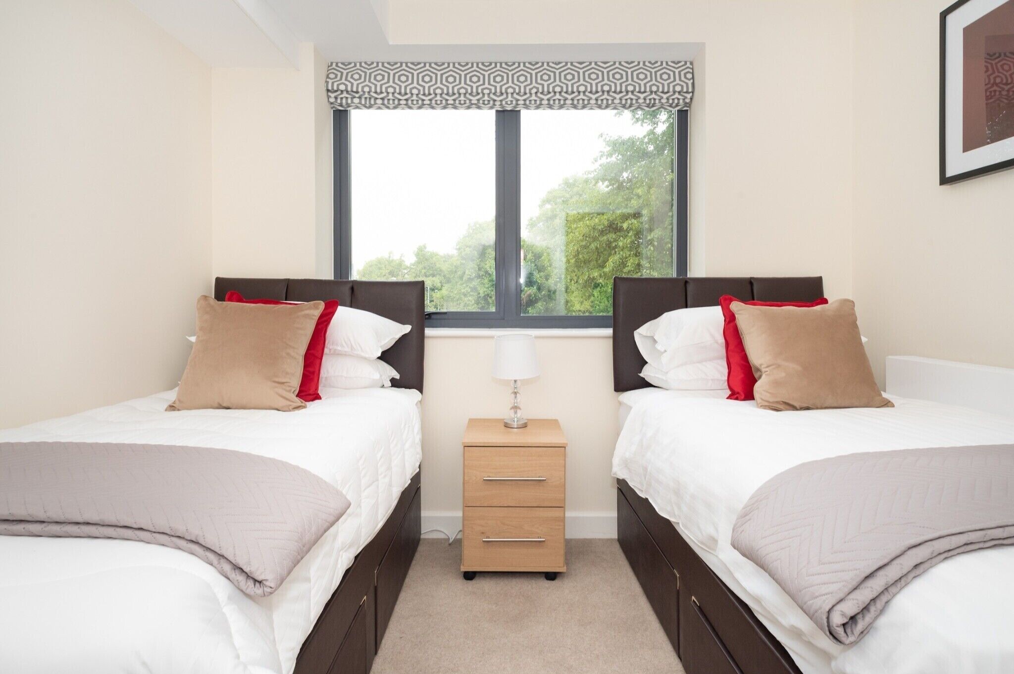 A twin room with two beds, a nightstand, and a window with a view of greenery.
