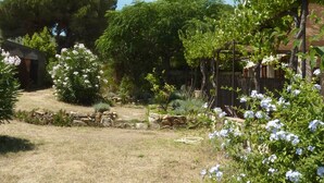 A garden with a variety of plants and trees, a stone wall, and a wooden pergola. - *** Les BOUTINELLES * Superb apartment in LA FERME DU MOULIN ROUX (Ramatuelle)