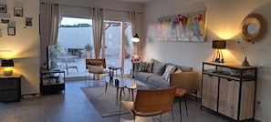A living room with a sofa, chairs, a table, a lamp, a painting, and a view through a glass door.