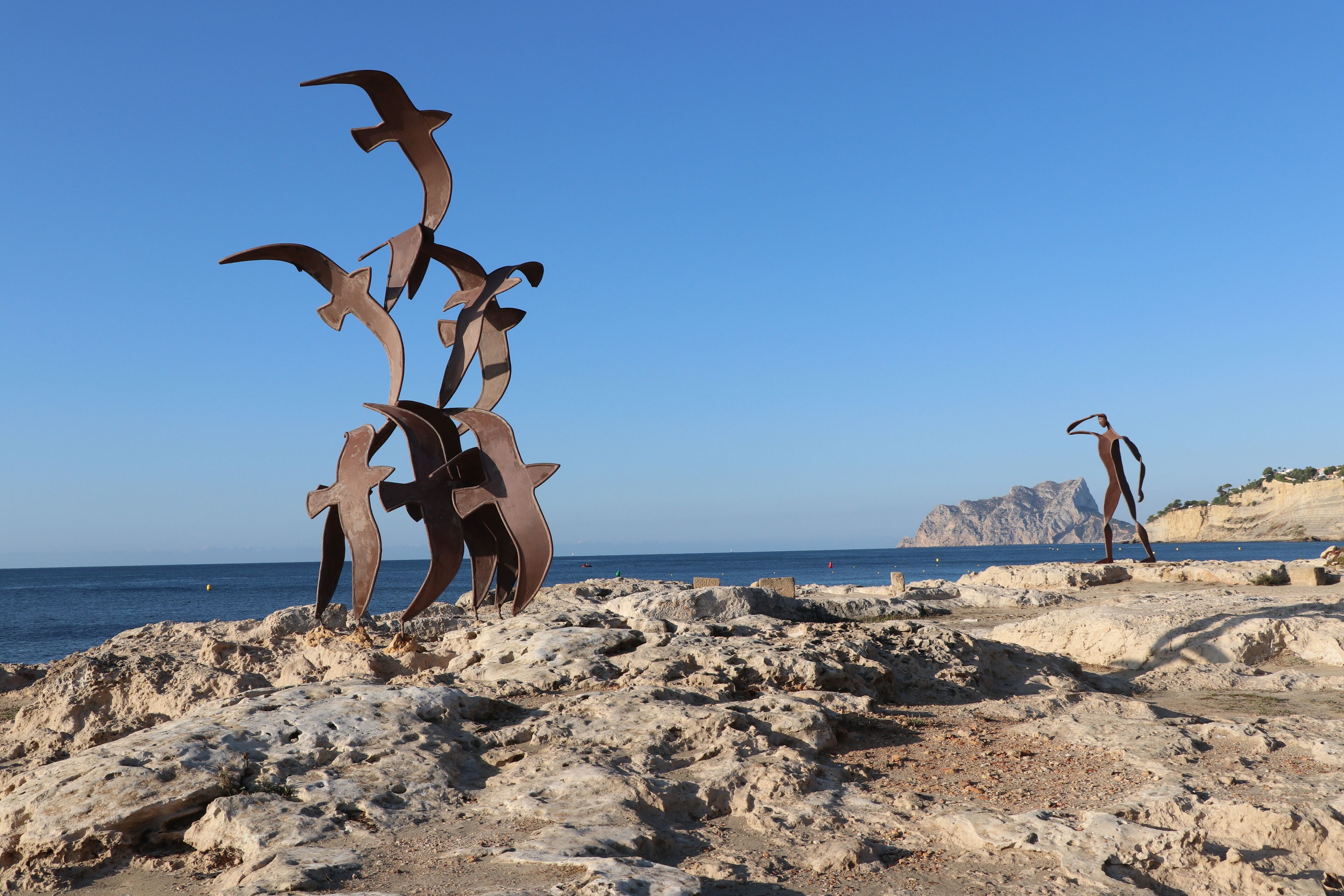 A rocky beach with a metal sculpture and a person walking.