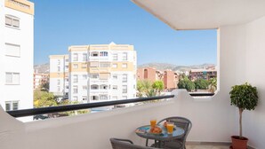Un balcón con mesa y sillas, una planta en maceta y vistas a edificios y montañas.