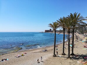 Een strand met palmbomen, mensen die zonnebaden en een helderblauwe lucht.