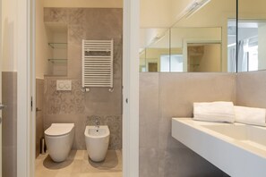 Un baño moderno con inodoro, bidé y un espejo grande sobre el lavabo.