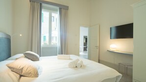 Hotellihuone, jossa on sänky, tyynyt, televisio, yöpöytä ja ovi, joka johtaa toiseen huoneeseen.