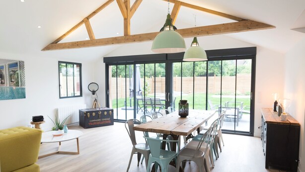 A spacious dining area with a wooden table and chairs, large windows, and a high ceiling with exposed beams. - Charming Villa with Garden near the beach (Tourgéville)