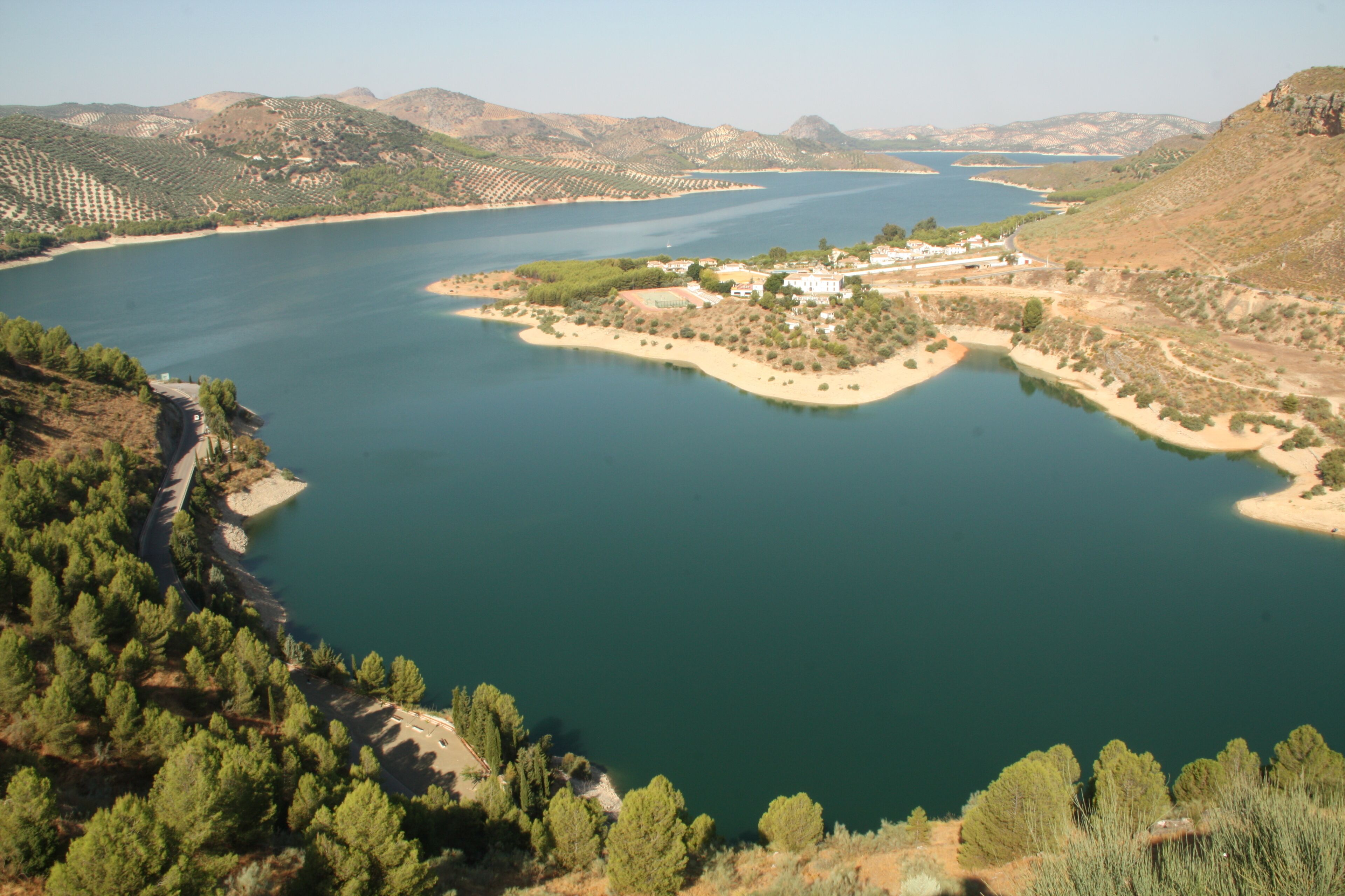 Paesaggio costiero con un ampio specchio d'acqua, una piccola isola con edifici e colline circostanti.