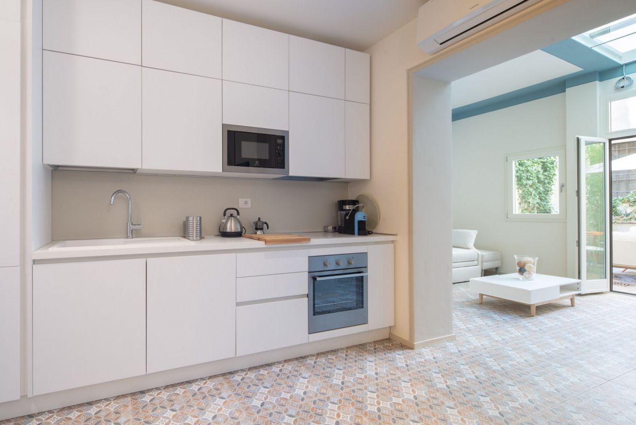 A modern kitchen with white cabinets, a microwave, a sink, and an oven. There is a coffee maker and a kettle on the counter. The floor has patterned tiles.