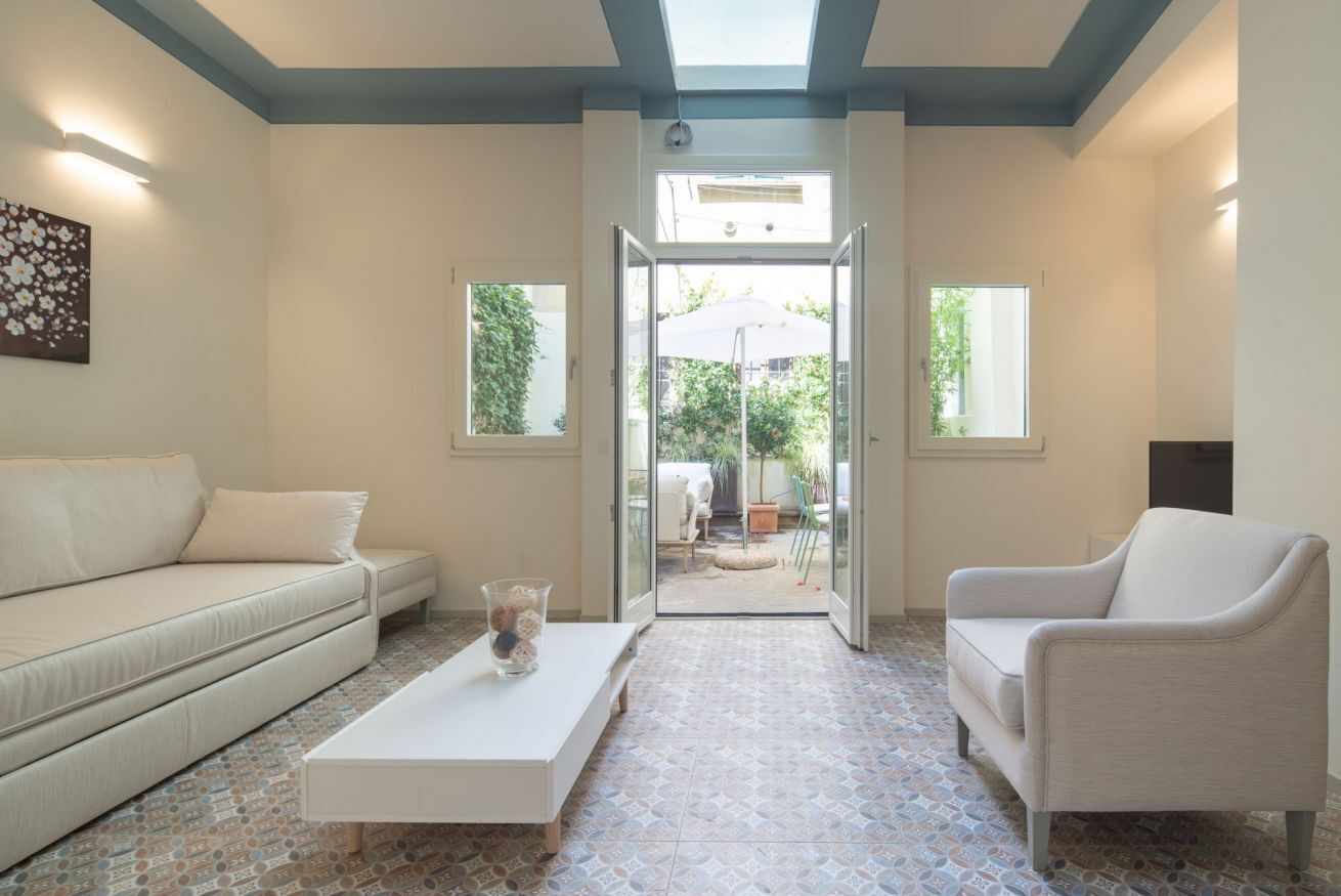A living room with a sofa, a coffee table, and a chair, with a view to an outdoor patio.