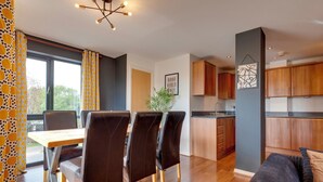 Una cucina moderna con mobili in legno, un'area pranzo con tavolo e sedie, e vista sull'esterno tramite ampie finestre.